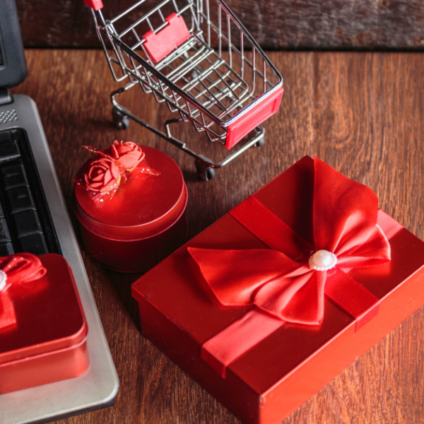 A laptop beside a red gift box and a shopping cart, symbolizing the ecommerce holiday rush.