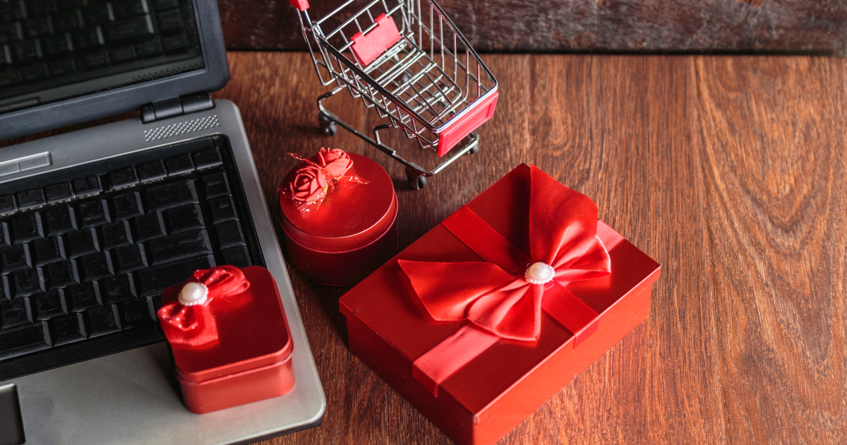 A laptop beside a red gift box and a shopping cart, symbolizing the ecommerce holiday rush.